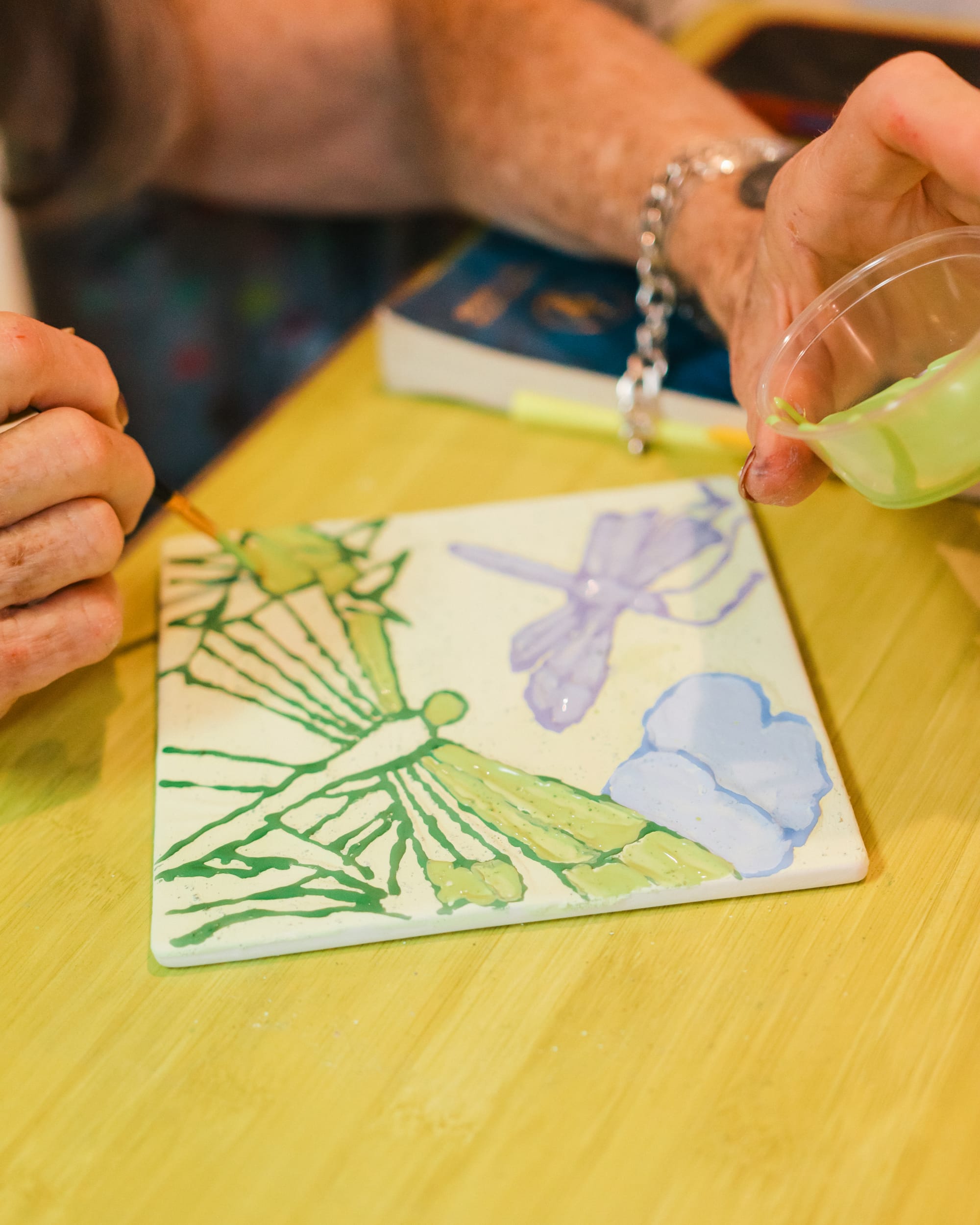 Elderly hands carefully painting a dragonfly onto pottery
